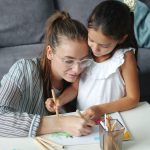 Adorable child and pretty young woman are drawing picture at home enjoying art and leisure time in house together. Family activities, children and happiness concept.